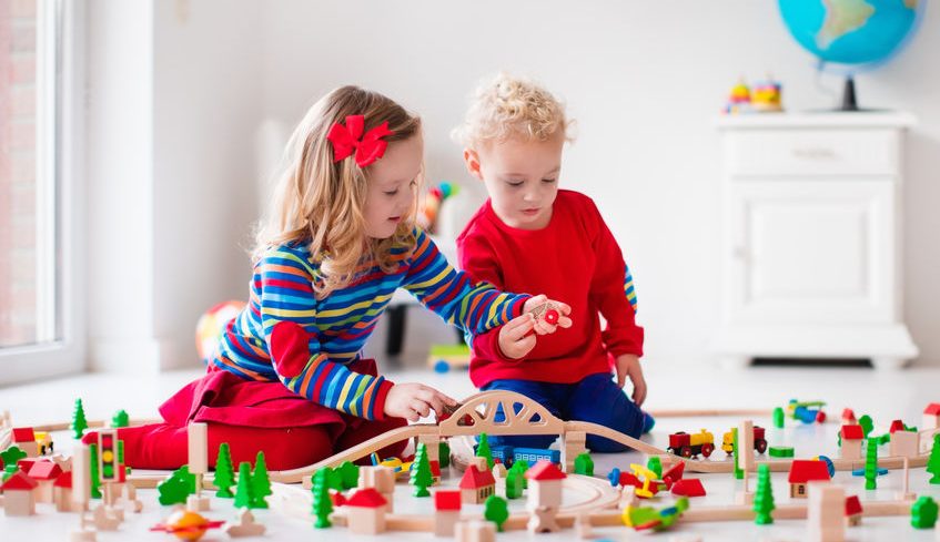 Children playing with wooden train. Toddler kid and baby play with blocks, trains and cars. Educational toys for preschool and kindergarten child. Boy and girl build toy railroad at home or daycare.